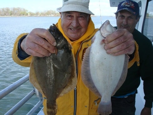 man holding two flounders on boat